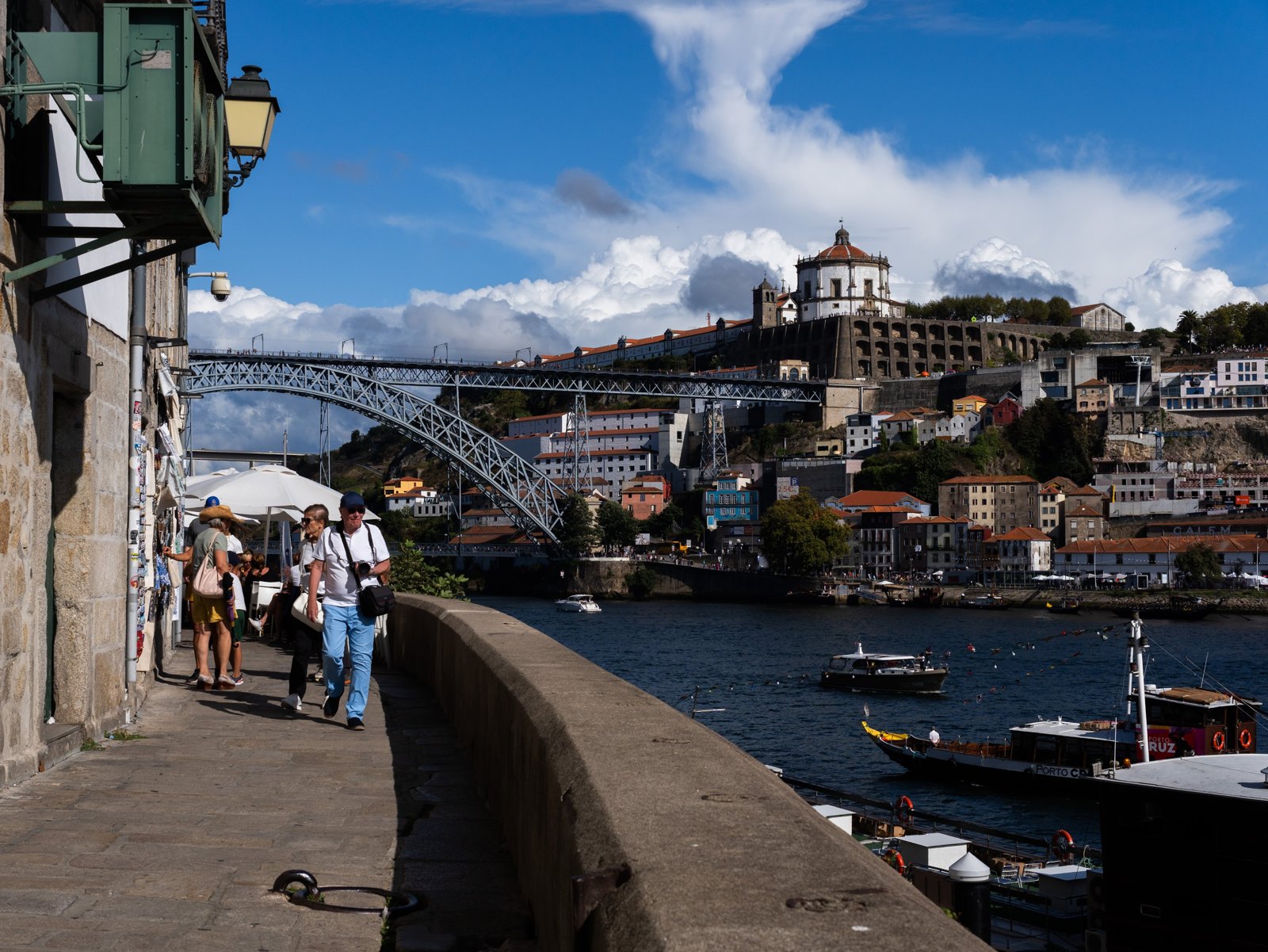 A riverside walkway with the bridge and hillside buildings across the water.